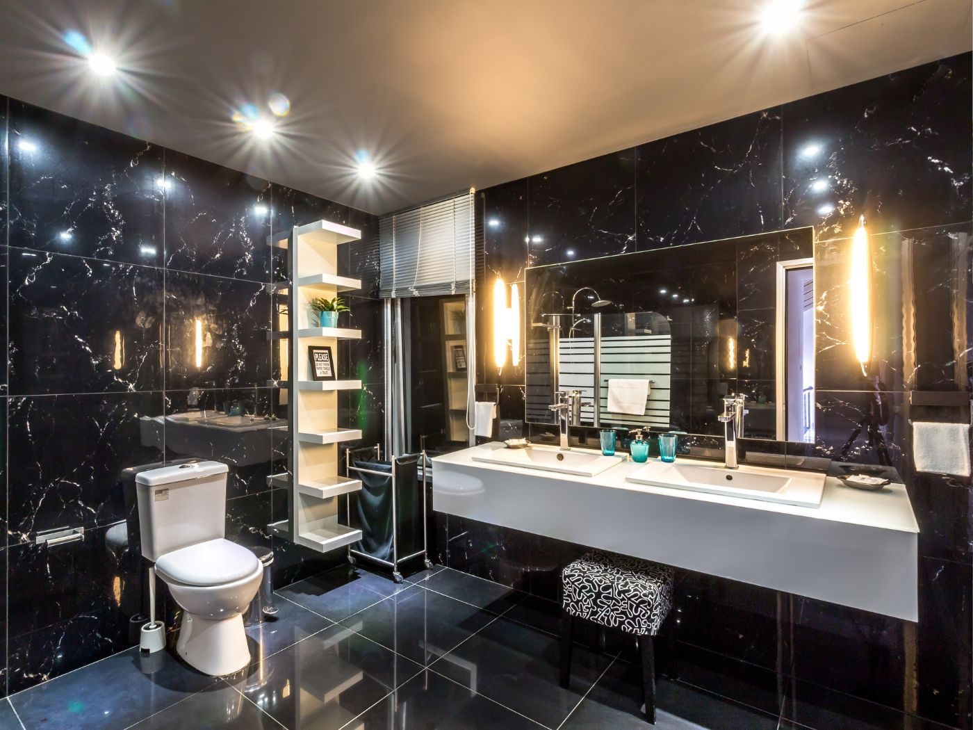 A bathroom lined in black marble-effect tile with twin basins and illuminated wall lights